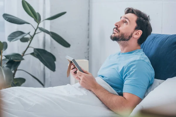 upset man lying in bed, looking up and holding photo frame at home