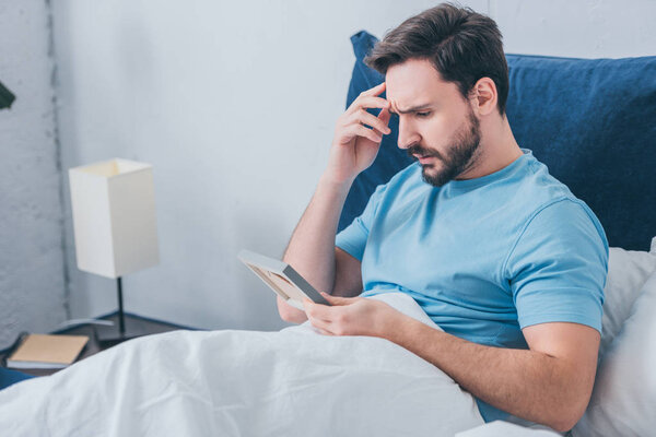 upset man lying in bed and holding photo frame at home