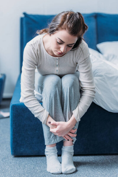 расстроенная женщина, обнимающая колени и сидящая дома на кровати
