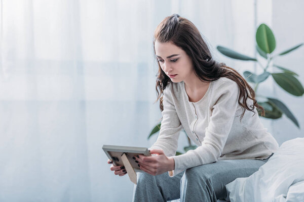 скорбящая женщина сидит на кровати и держит фотографию рамку дома с копировальным местом
