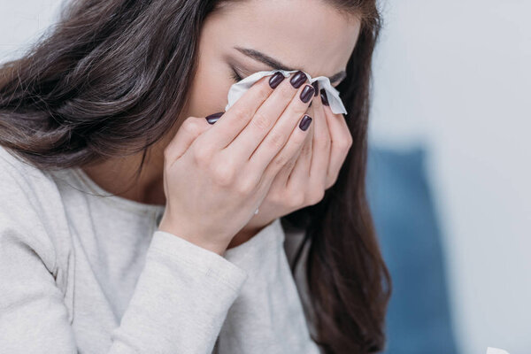 selective focus of grieving woman covering face with hands and crying at home