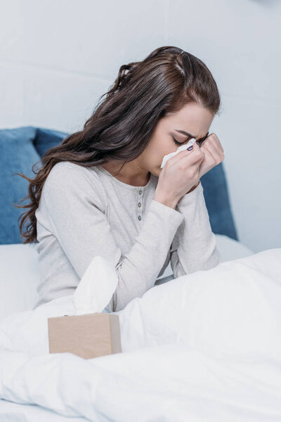 woman lying in bed with tissue box, crying and wiping tears 