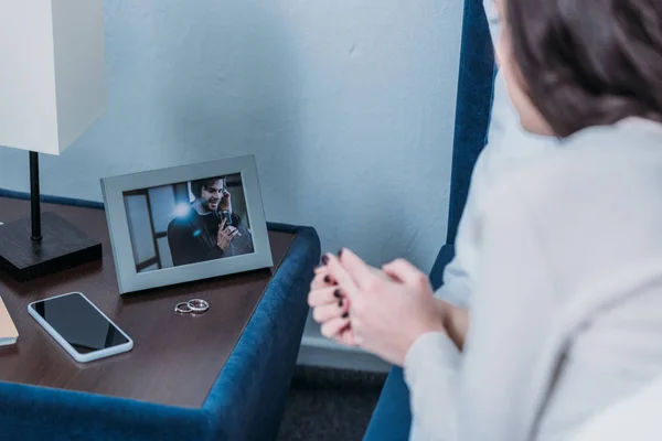 裁剪的妇女看着相框与男人和结婚戒指的照片在床头柜上 — 图库照片