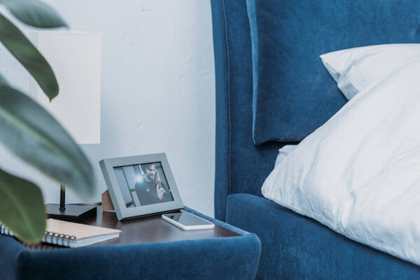 selective focus of photo frame with picture of man, notebook and smartphone on bedside table