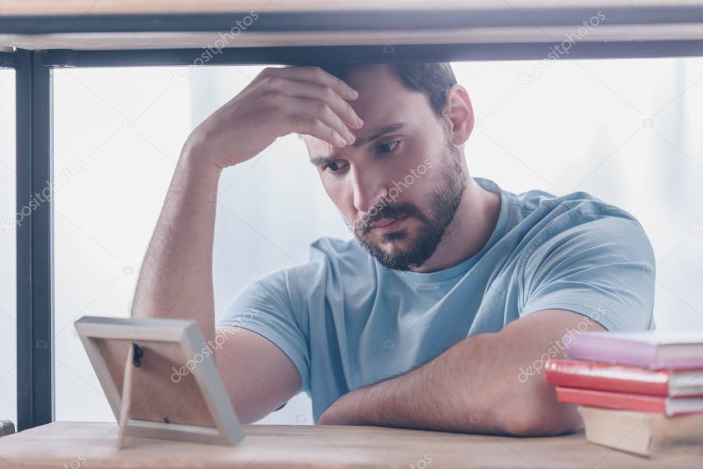 upset man touching head while looking at photo frame at home