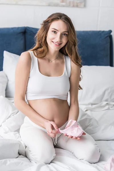 Mujer Embarazada Dichosa Sentada Cama Sosteniendo Ropa Bebé Rosa —  Fotos de Stock