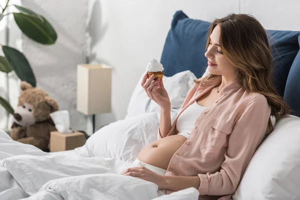 Ευχαριστημένος Έγκυος Γυναίκα Ξαπλωμένη Στο Κρεβάτι Και Κρατώντας Cupcake — Φωτογραφία Αρχείου