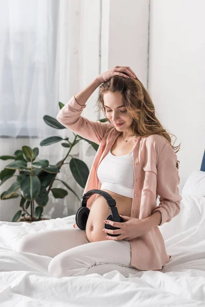 Αρκετά Έγκυος Γυναίκα Που Κάθεται Στο Κρεβάτι Ακουστικά Την Κοιλιά — Φωτογραφία Αρχείου