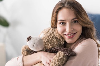 Gülümseyen kadın kucaklayan oyuncak ayı ve kamera için arıyorsunuz