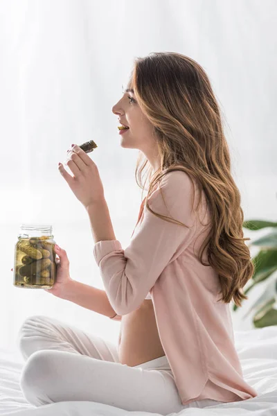 Side view of long-haired pregnant woman eating pickles on bed — Stock Image Side View Long Haired Pregnant Woman Eating Pickles Bed Royalty Free Stock Photos