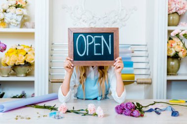 beautiful female flower shop owner holding chalkboard with 'open' lettering in front of face clipart