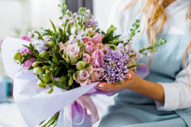 cropped view of female florist holding bouquet with lilac and roses in flower shop clipart
