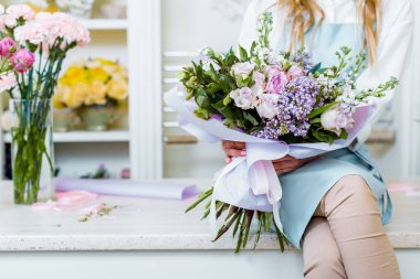 tezgahın üzerinde oturuyor ve leylak ve gül buket çiçek dükkanında tutan kadın çiçekçi kırpılmış görünümünü