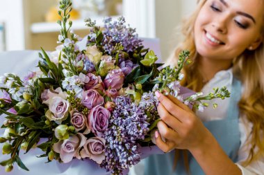 smiling female florist arranging bouquet with lilac and roses in flower shop clipart
