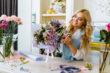 beautiful smiling female florist in apron arranging bouquet in flower shop  clipart