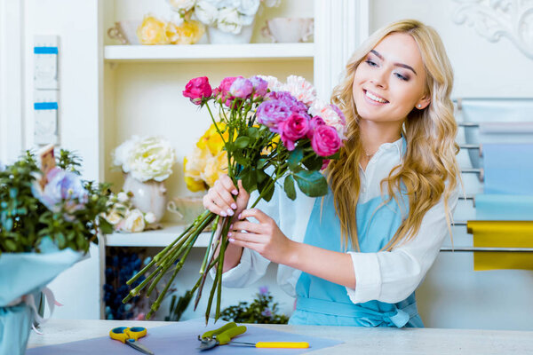 beautiful smiling female florist arranging bouquet in flower shop