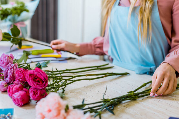 обрезанный вид женщины-флориста, сидящей за столом с розовыми розами и гвоздиками во время оформления букета
