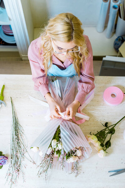 top view of female florist in glasses arranging bouquet in flower shop