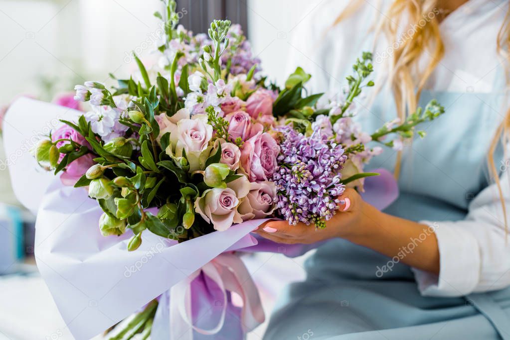 cropped view of female florist holding bouquet with lilac and roses in flower shop