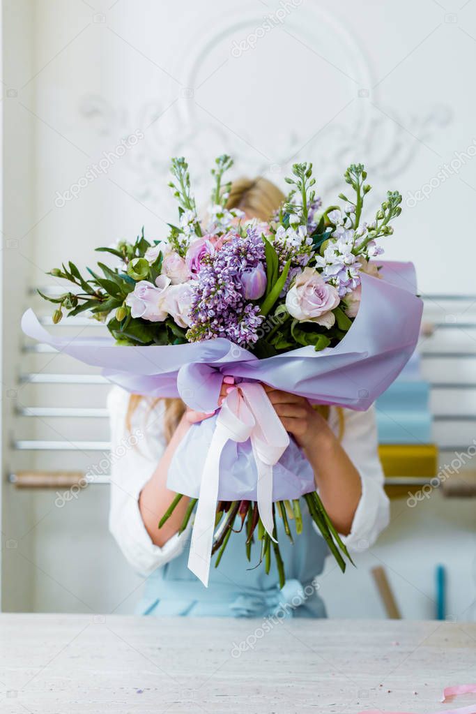 woman holding flower bouquet with roses and lilac in front of face