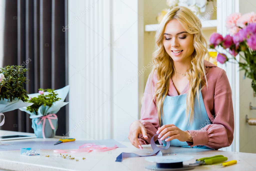 beautiful smiling female florist at counter with decorative supplies and tools in flower shop