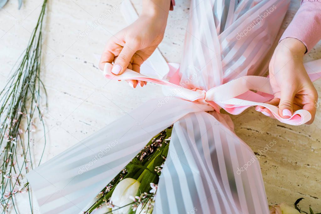 partial view of female florist tying bow with ribbon while wrapping flower bouquet 