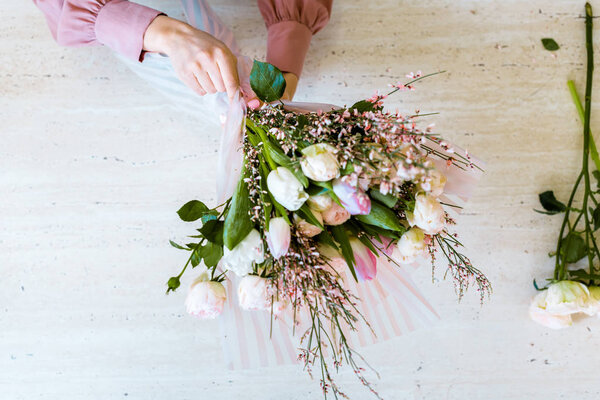 top view of female florist arranging bouquet with white tulips and roses on table