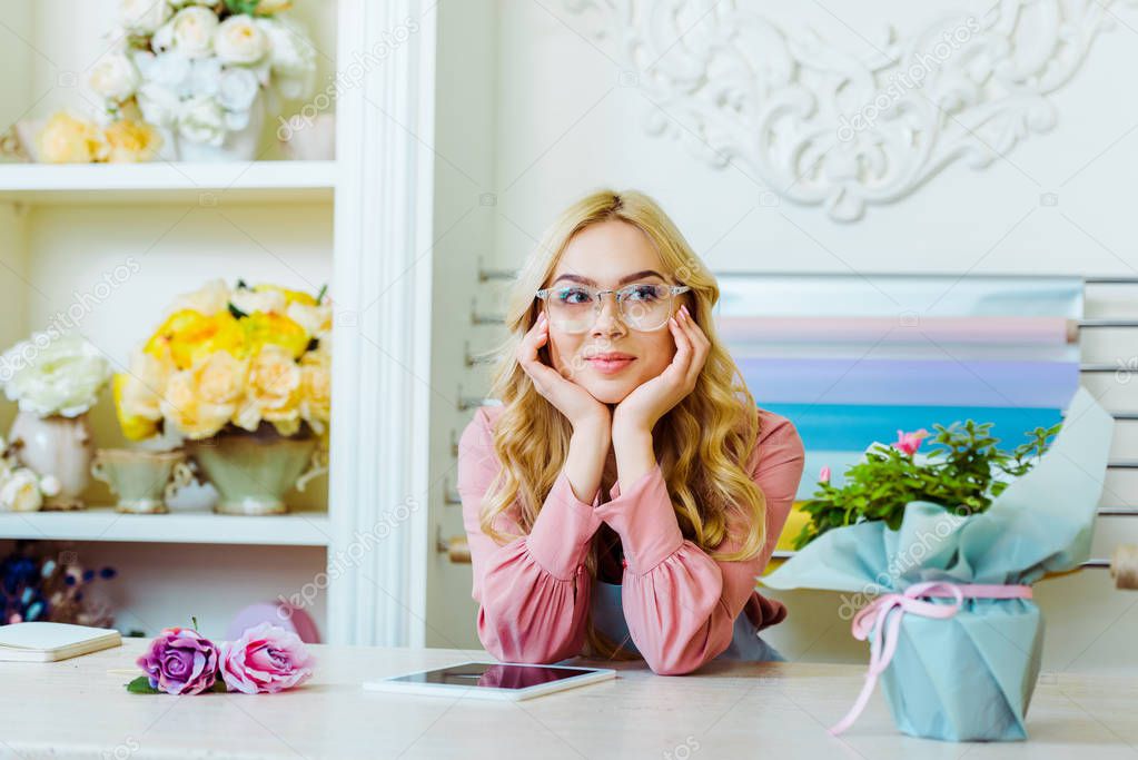 beautiful female flower shop owner in glasses with digital tablet propping face with hands at counter