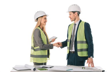 architects in safety vests and hardhats making deal and shaking hands, isolated on white