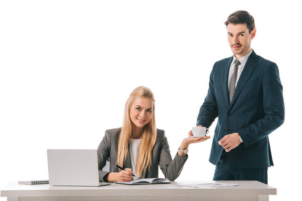 handsome secretary brought cup of coffee for smiling businesswoman at workplace with laptop, isolated on white