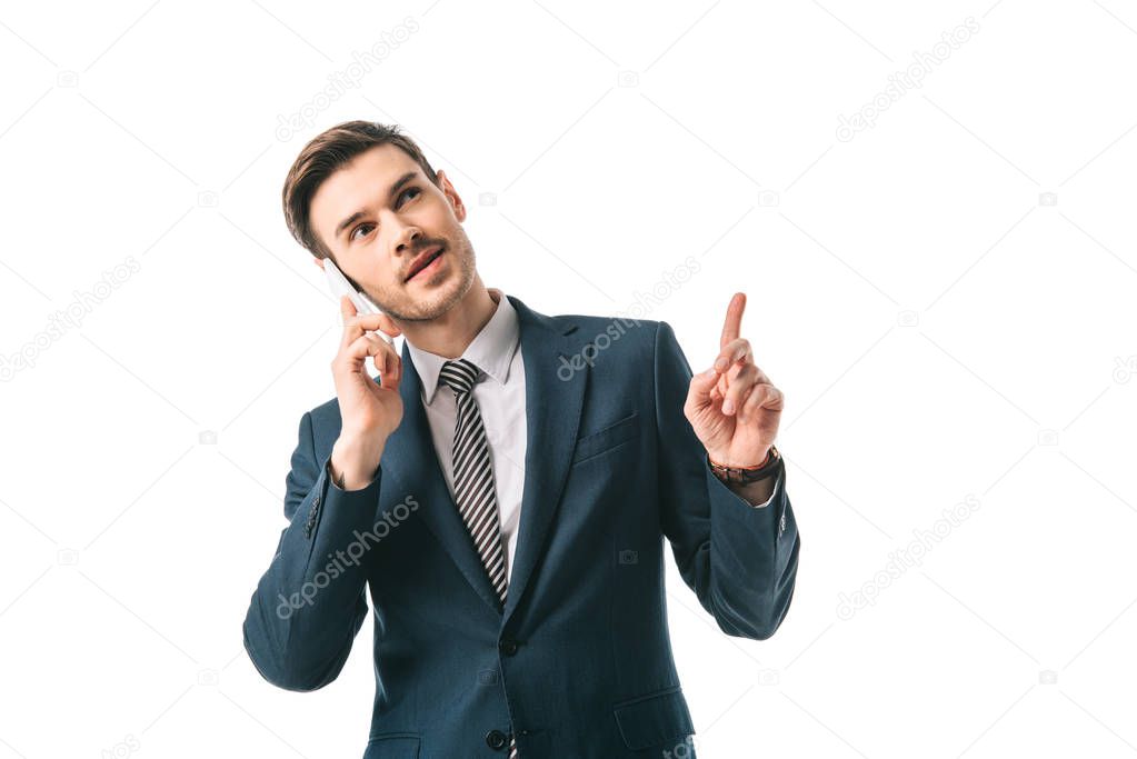 handsome businessman having idea and pointing up while talking on smartphone isolated on white