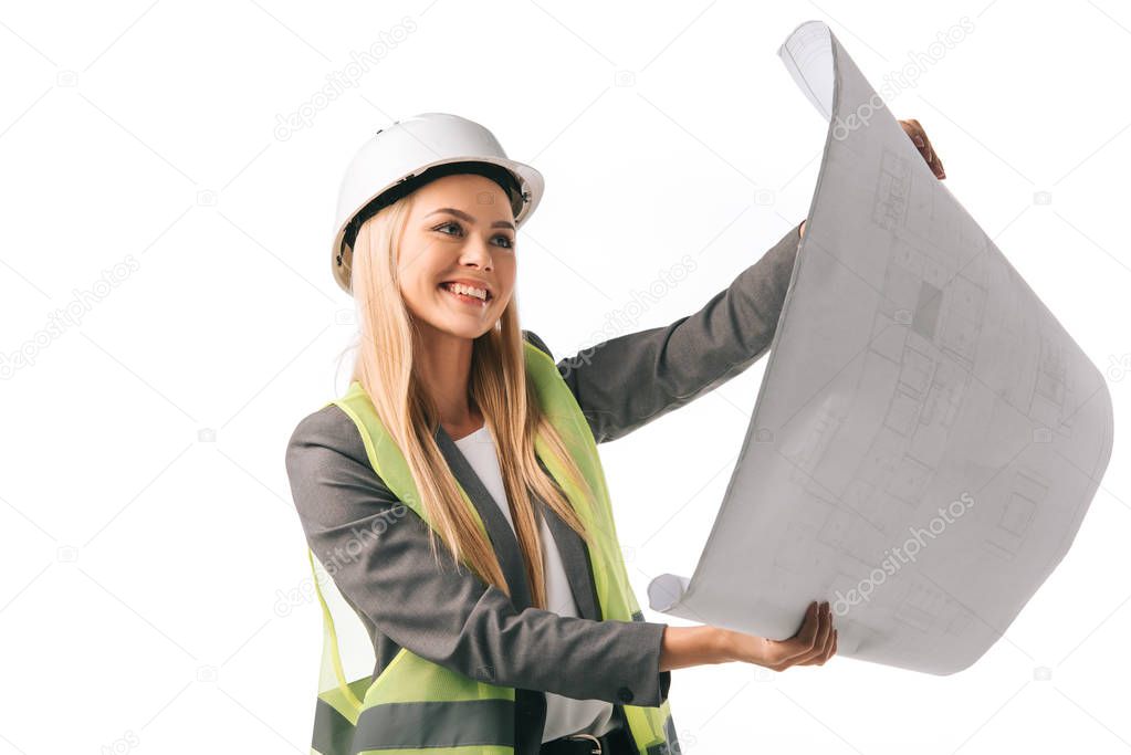 cheerful female architect in safety vest and hardhat working with blueprint, isolated on white