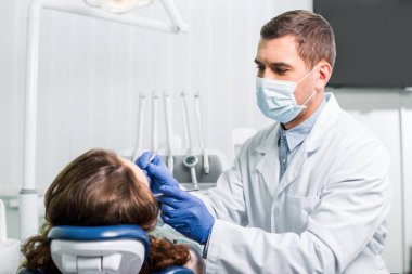 dentist in mask working with woman in latex gloves in dental clinic clipart