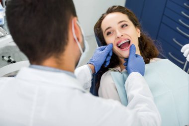 diş hekimi yakınındaki incelenmesi sırasında ağız açma kaşlı ayraçlar içinde neşeli kadın seçici odak