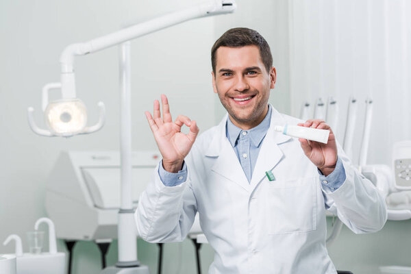dentist holding toothpaste and showing ok sign in dental clinic