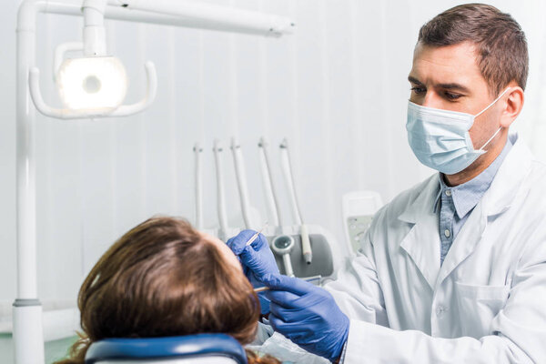 dentist in latex gloves and mask working with woman in clinic