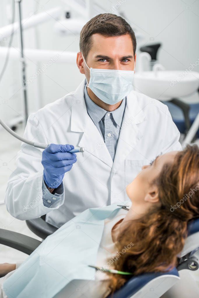 selective focus of dentist in white coat and mask examining female patient