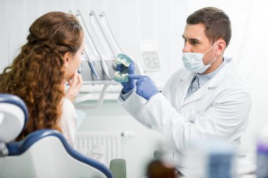 seçici odak bir dişçi diş model Bayan hasta yakınındaki parmak ile işaret maskesi ve lateks eldiven