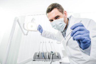 lateks eldiven ve maske diş lamba ve diş aleti elinde tutan diş hekimi