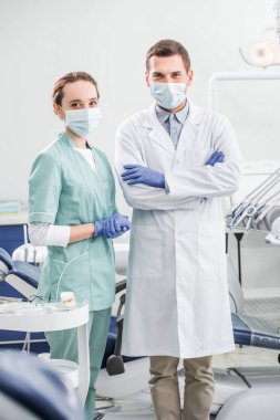 selective focus of dentists in masks standing with crossed arms in dental clinic clipart