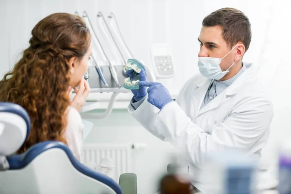 メスの患者の近くの歯のモデルを指で指しているマスク ラテックス手袋で歯科医の選択と集中 — ストック写真