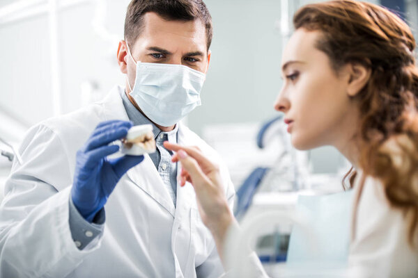 selective focus of dentist in latex gloves holding teeth model near female patient
