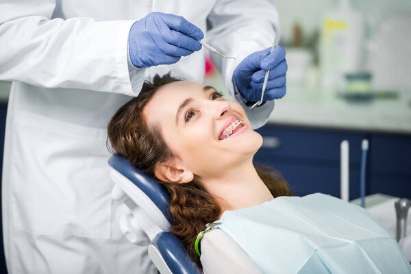 cropped view of dentist in latex gloves examining cheerful woman in braces 