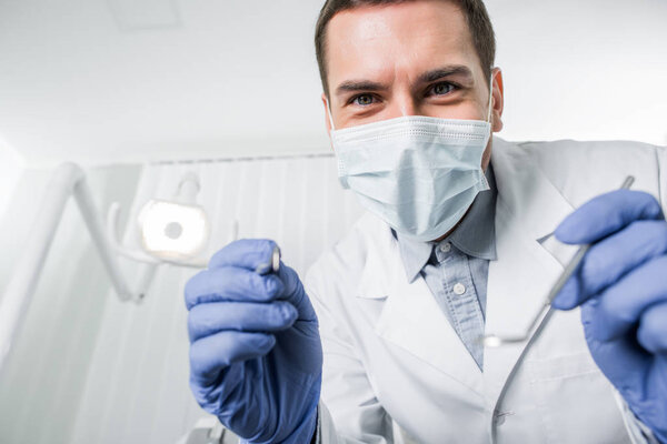selective focus of dentist in latex gloves and mask holding dental instruments in hands