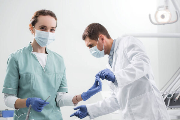  стоматолог, дающий стоматологический инструмент женщине-коллеге в маске
