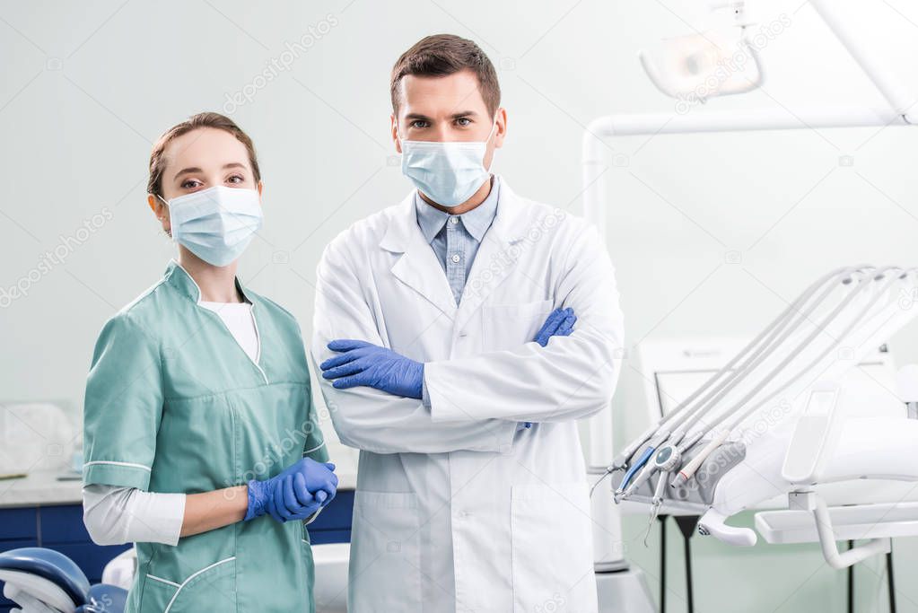 dentists in masks standing with crossed arms in dental clinic