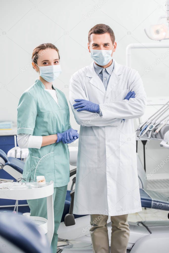 selective focus of dentists in masks standing with crossed arms in dental clinic