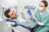dentist in mask holding dental instruments near cheerful patient in dental clinic