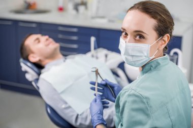 seçici odak bir hasta yakınındaki diş enstrüman tutan maskeli kadın dişçi 