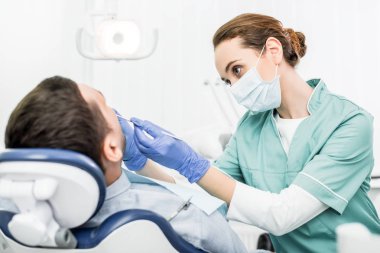 Diş Kliniği hastada ile çalışırken diş aletleri tutan maskeli kadın diş hekimi